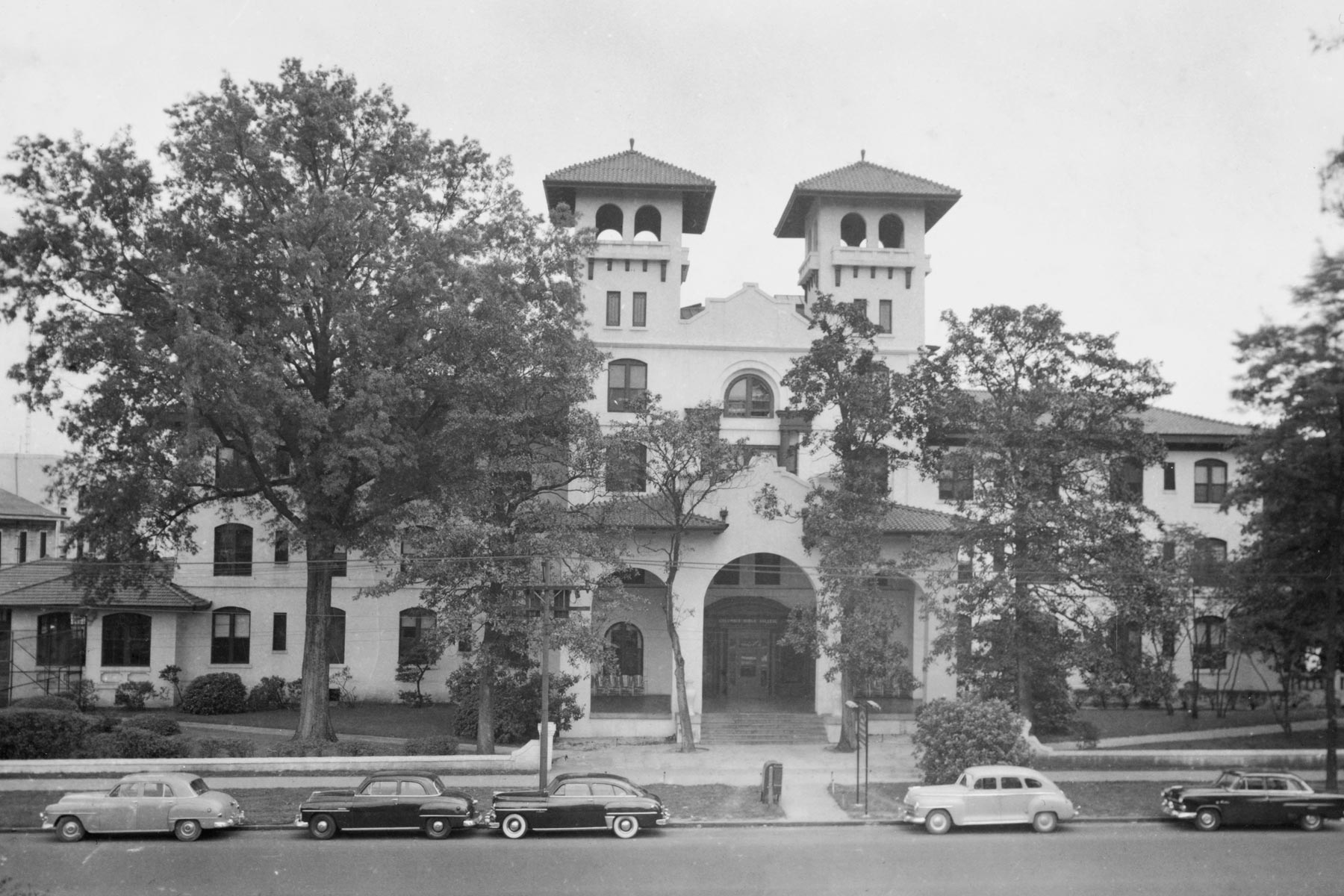 Historic black and white photo of a Columbia International University building with trees and cars in front.