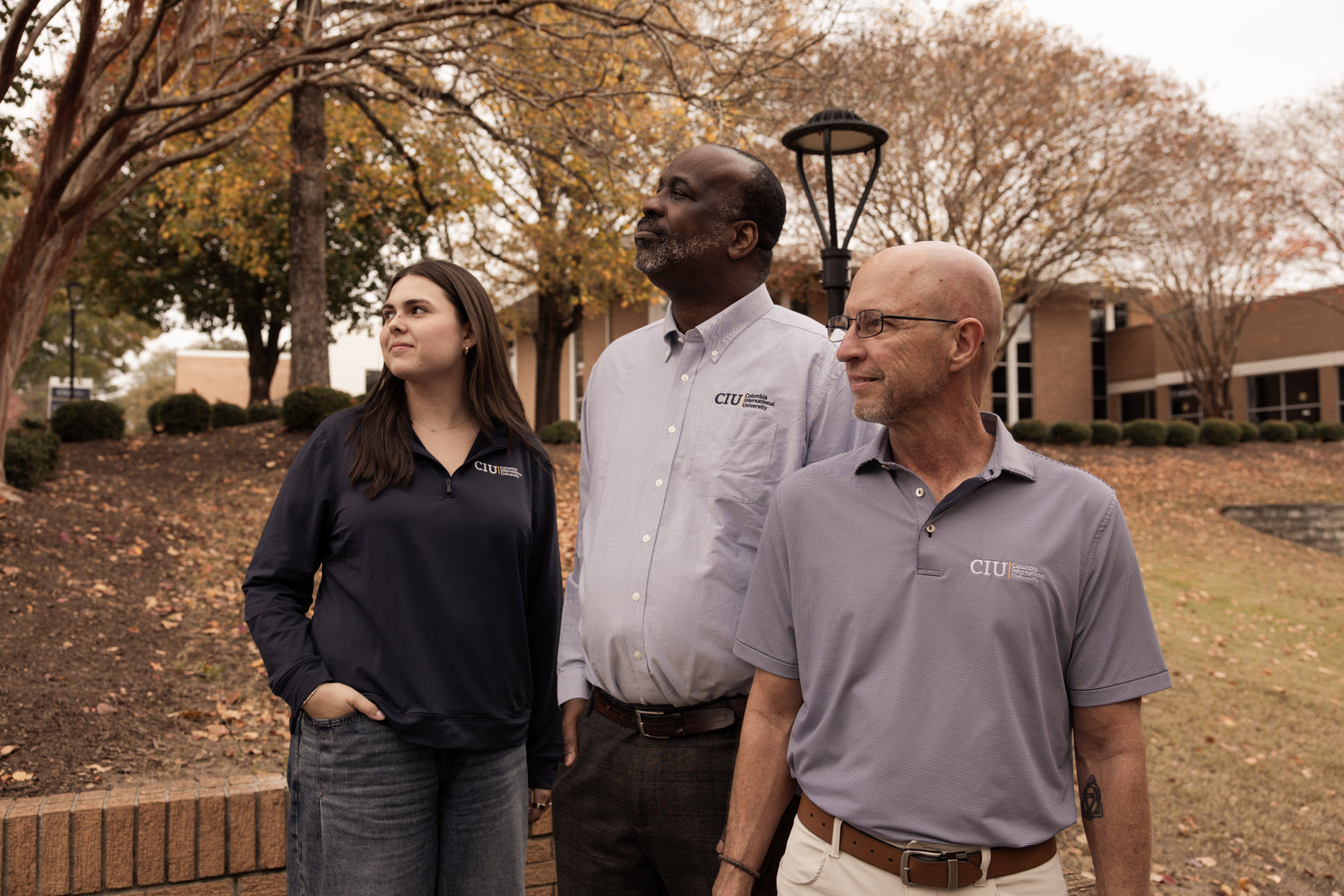 Three people standing outdoors in CIU professional merch with trees and campus buildings in the background.