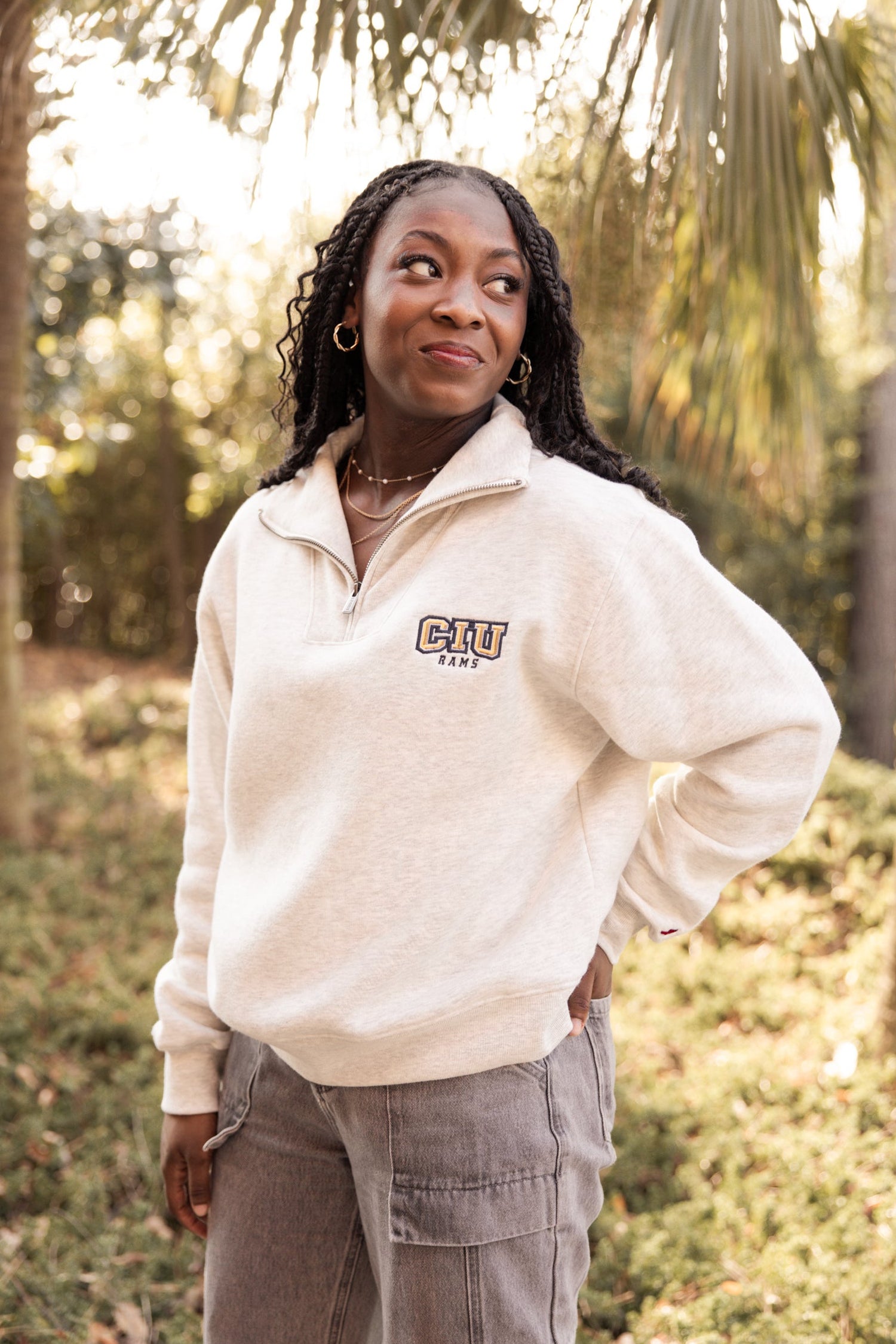 Woman wearing a cream Columbia International University zip up with trees in the background.