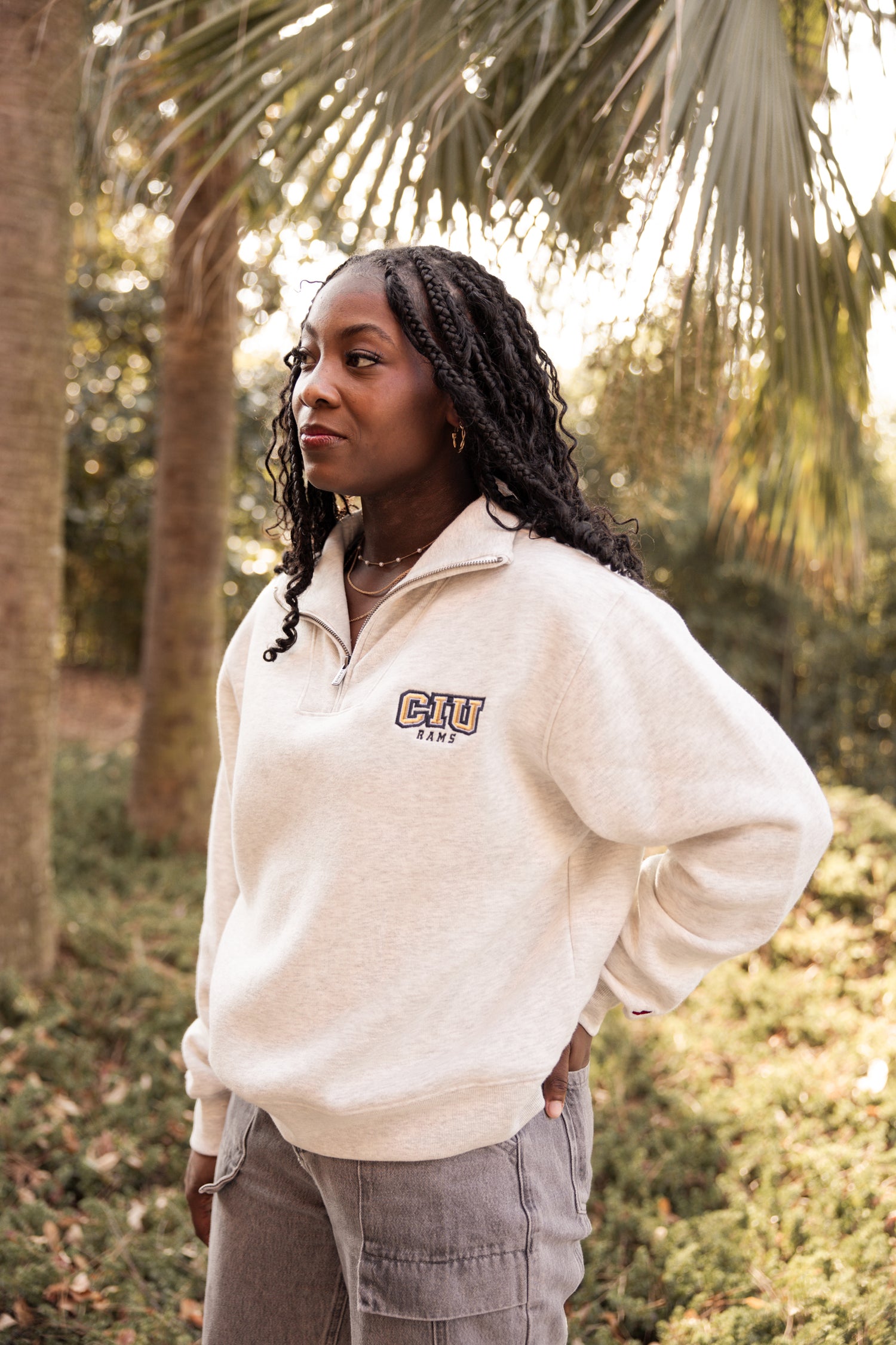 Woman wearing a cream Columbia International University zip up with trees in the background.