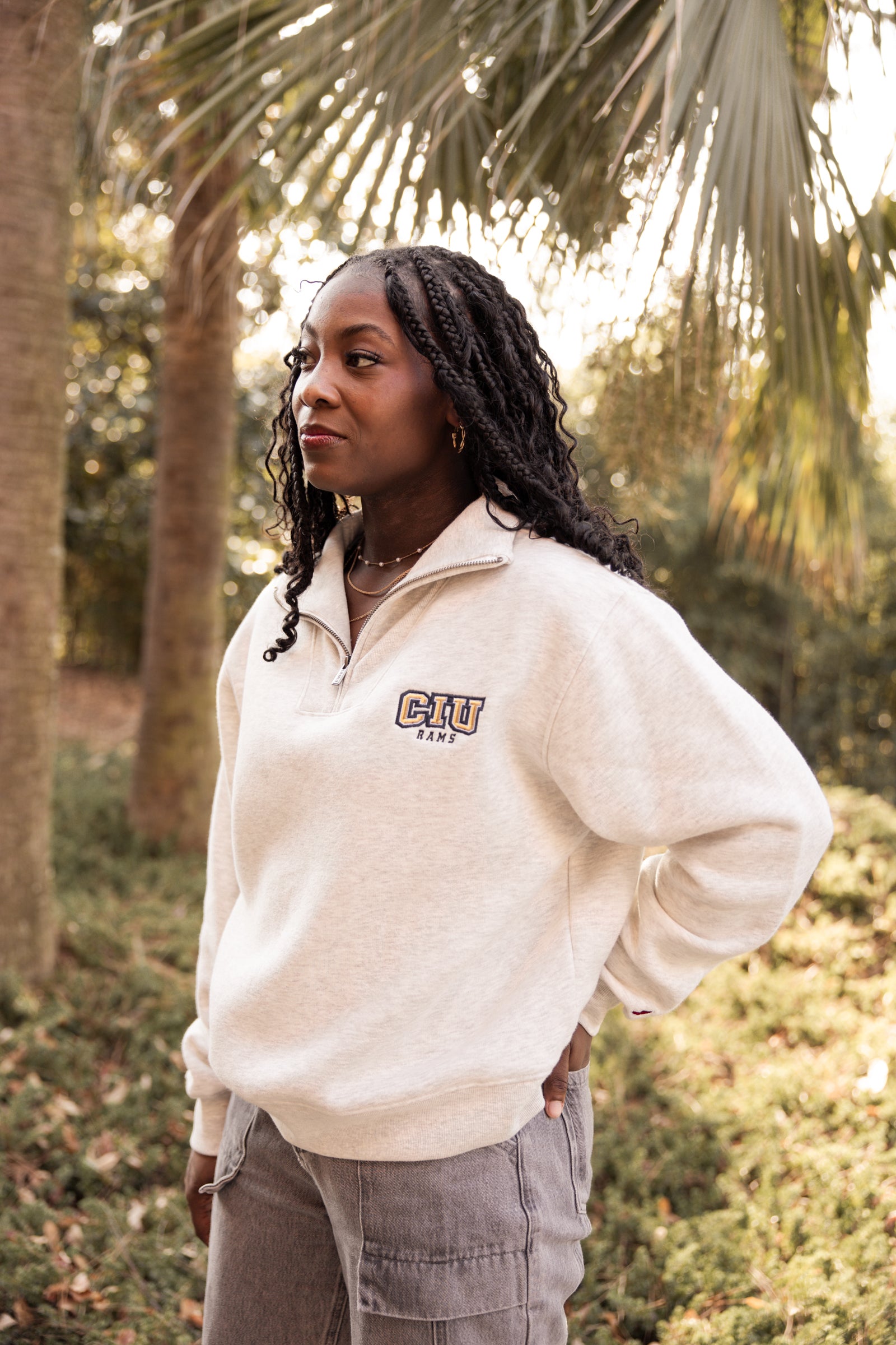Woman wearing a cream Columbia International University zip up with trees in the background.