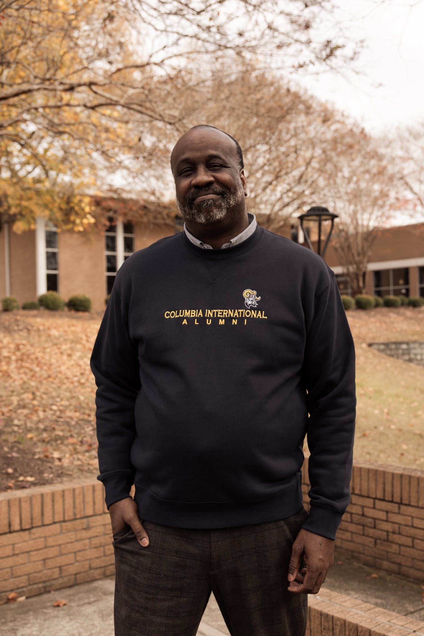 Man wearing a Columbia International Alumni sweatshirt standing outdoors.