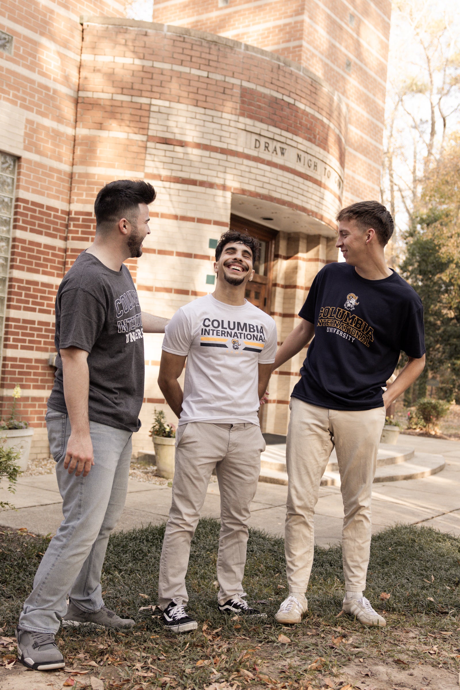 Three men standing outside a brick building, wearing Columbia International University shirts.