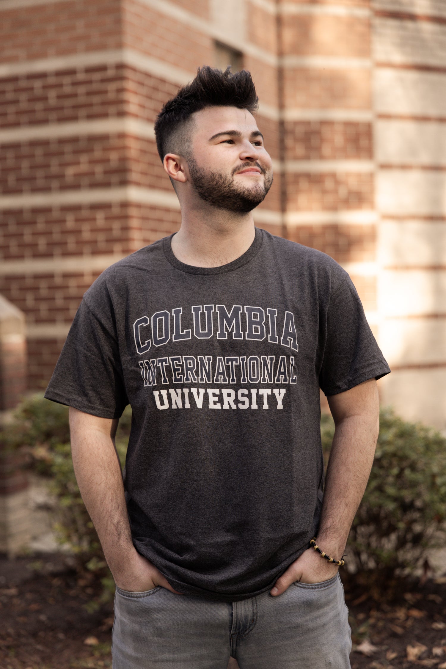 Man wearing a Columbia International University t-shirt standing in front of a brick building.