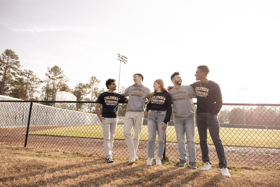 Five students wearing Columbia International University merch standing near a baseball field.