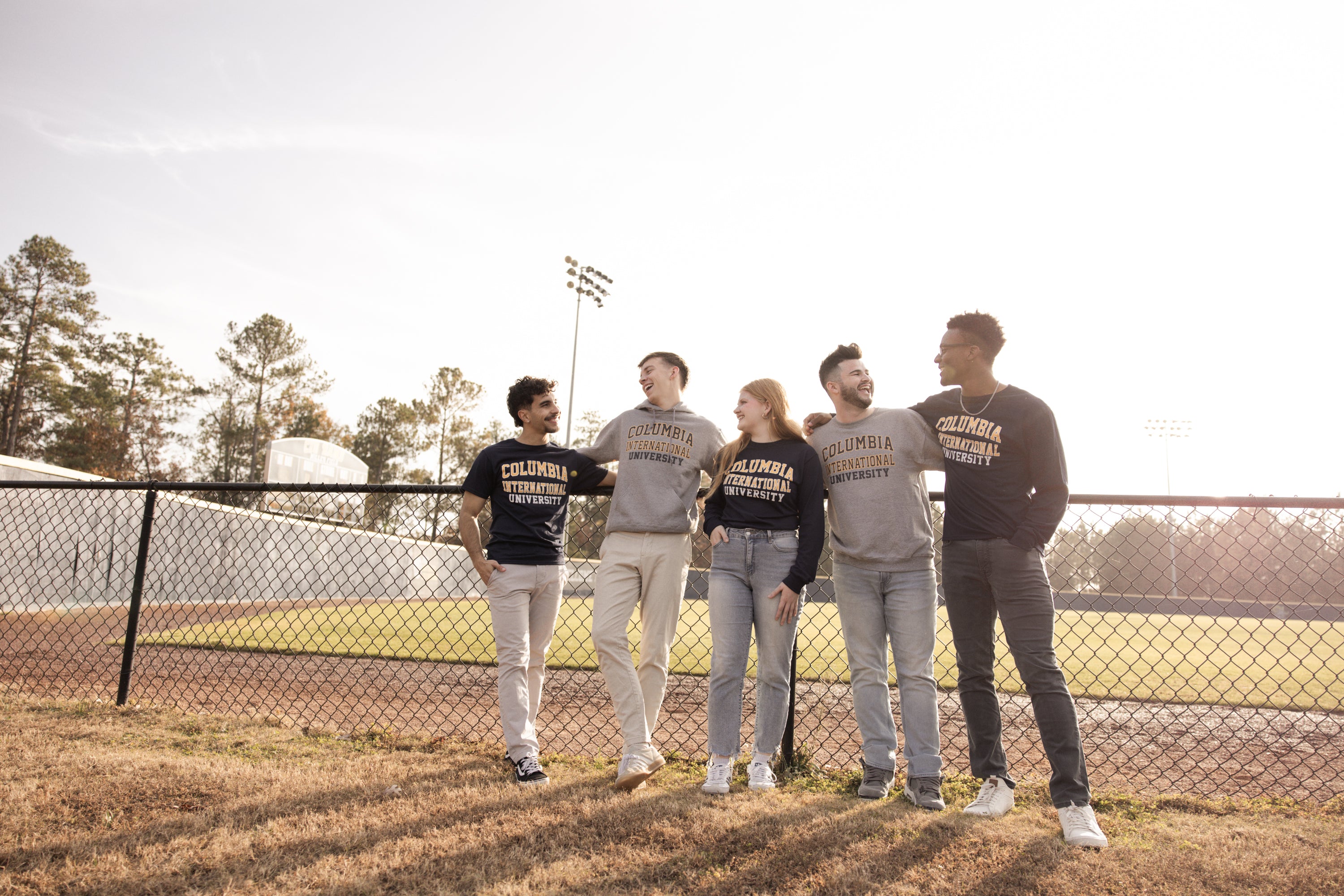 Five students wearing Columbia International University merch standing near a baseball field.